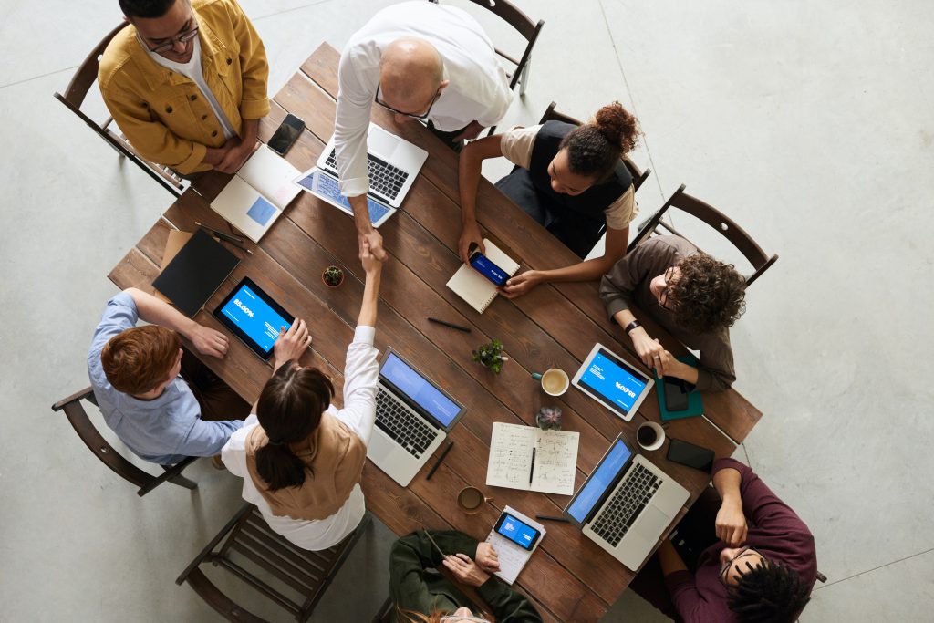 8 employees gather around a table on their laptops discussing employee engagement ideas.