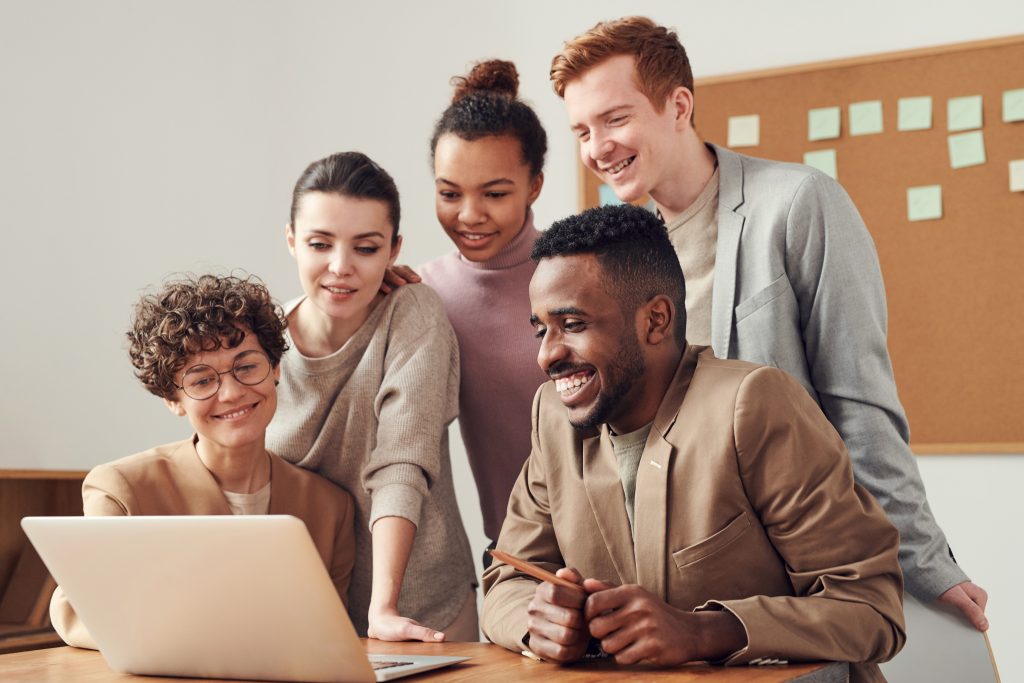 5 employees working on a laptop smiling.