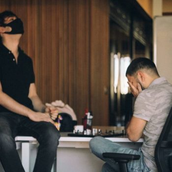 An employee sat on his desk sadly covering his face with his hands, suffering from mobbing