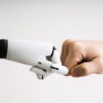 A robot hand and a human hand clashing fists in a collaborative manner