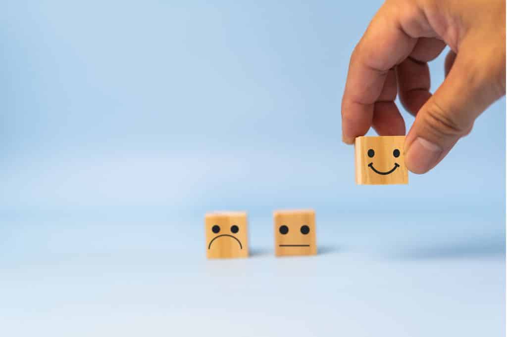 Tres bloques de madera con caras reflejando las respuestas de una encuesta de satisfacción laboral